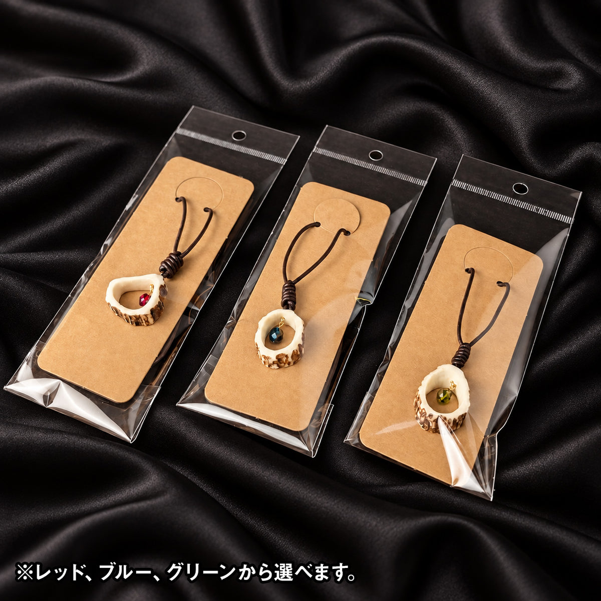 黒いシルクの上に並べた、個別包装の鹿角ビーズネックレス3色